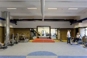 De voormalige transformatorhal is nu oefenruimte voor fysiotherapie. Twee blauwe stalen balken met transportmechaniek zijn behouden gebleven