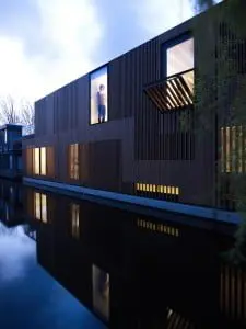 Watervilla nabij het Olympisch stadion in Amsterdam, ontwerp Framework Architecten & Studio Prototype. Het contact tussen water en woning staat centraal in het ontwerp. De verticale lattenstructuur in de gevels zorgt voor de gewenste privacy, maar ook voor een subtiel lichtspel in de woning zelf. Foto: Jeroen Musch