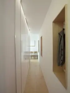 3.Vanaf de entree loopt een gang van 80 cm breed naar de voorkant van de woning. Rechts zijn op drie plekken nissen aangebracht om de lange wand te breken en het ruimtegevoel te vergroten. Berging, wc, douche en kledingkast zitten verborgen achter een wand van lichtdoorlatend polycarbonaat. De lichtlijn achter de deuren verlicht ook de gang.