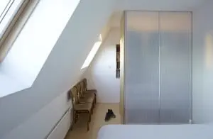 4. De achterwand van de kledingkast scheidt de slaapkamer van de gang. Aan weerszijden van het tweepersoonsbed hangt een peertje laag boven de vloer. Het lange snoer loopt via een haakje in een boog naar het elektrapunt in het plafond. De stoelen kreeg Dooghe van zijn Vlaamse oma. ‘Via de Velux ramen kan ik zo makkelijk bij mijn kruiden- en aardbeienplantjes in de dakgoot.’