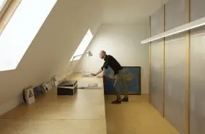 6.In de werkkamer staan drie multiplex werkbladen op schragen tegen het dakbeschot. ‘Het achterliggende idee is, dat de vloer doorloopt en als het ware tegen de muur omklapt,’ legt Dooghe uit. In een dichtgemaakte opening naar de gang maakte Dooghe een opbergnis voor ordners. De achterwand van de boekenkast tussen werkkamer en keuken gebruikt hij als projectbord. De twee lichtbakken van Philips zijn precies even breed als de kast.