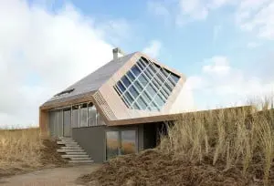 Vanuit het noordwesten, grote vensters zorgen voor een intense beleving van duinen en zee. De gevel met de lichte helling vormt als vanzelf de loungebank op het terras