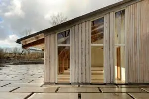 Een deel van de gevels is bekleed met houten delen met de schors er nog aan en balken lopen van het interieur door naar buiten.