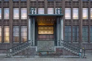 Hoofdentree met bronzen deuren, omlijst door Frans kalksteen. De entree is uitgerust met een verhoogd trapbordes, natuurstenen treden en bronzen leuningen. Aan de voorzijde van het bordes is een bronzen embleem van de Nederlandse Handelsmaatschappij, ontworpen door N. Klaassen, aangebracht. 