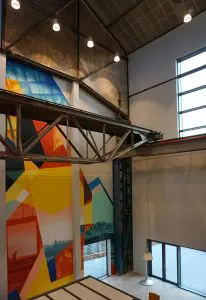 In de vide achter de hoofdentree hangt een oude kraan en zijn de oude spanten zichtbaar. Een muurschildering verwijst naar de historie van de plek.