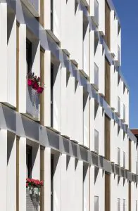 Uitkragende kaders van wit aluminium rondom de ramen creëren dieptewerking met schaduwen en reliëf op de vlakke gevel. Kijk je recht op de gevel, dan zie je vooral de houten bekleding. Kijk je er zijdelings op, dan is alles wit. Daarnaast zorgen de kaders van binnenuit voor extra stevigheid en geborgenheid