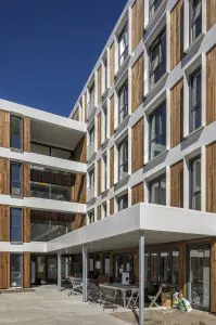 Het L-vormige gebouw wordt ontsloten via een centrale ingang in de hoek waar de twee vleugels samenkomen. In dezelfde hoek bevinden zich op de eerste drie verdiepingen gemeenschappelijke bewonersruimtes en op de begane grond een grote ruimte met overkapt terras waar omwonenden ook gebruik van maken. Deze ruimtes zijn bedoeld om het communitygevoel versterken