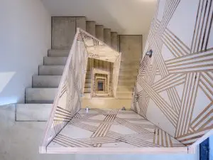 Voor de binnentrap
bedacht het
Eindhovense
ontwerperscollectief
Envisions
een streeppatroon
over de
alle vier verdiepingen
langs de
dichte leuning
in betonplex
omhoog loopt,
een visuele
referentie naar
de gestreepte
buitengevel
