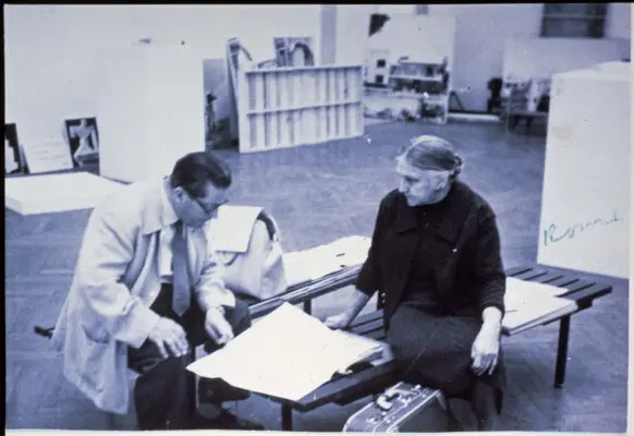 084F376
Gerrit Rietveld links en Truus Schröder rechts zittend op banken; GR kijkend naar uitgevouwen kaart; vóór TS staat een koffertje op de grond;
foto Roeland van der Hidde
scan van reproductie van foto op dia